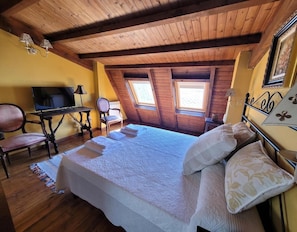 Une chambre confortable située dans les combles, avec un lit, une télévision, un bureau et deux fenêtres.