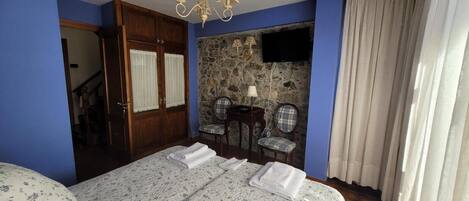Un dormitorio con cama, candelabro, pared de piedra, televisor y ventana con cortinas.