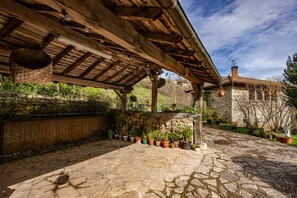 A stone-paved courtyard with a wooden pergola, potted plants, and a stone wall.