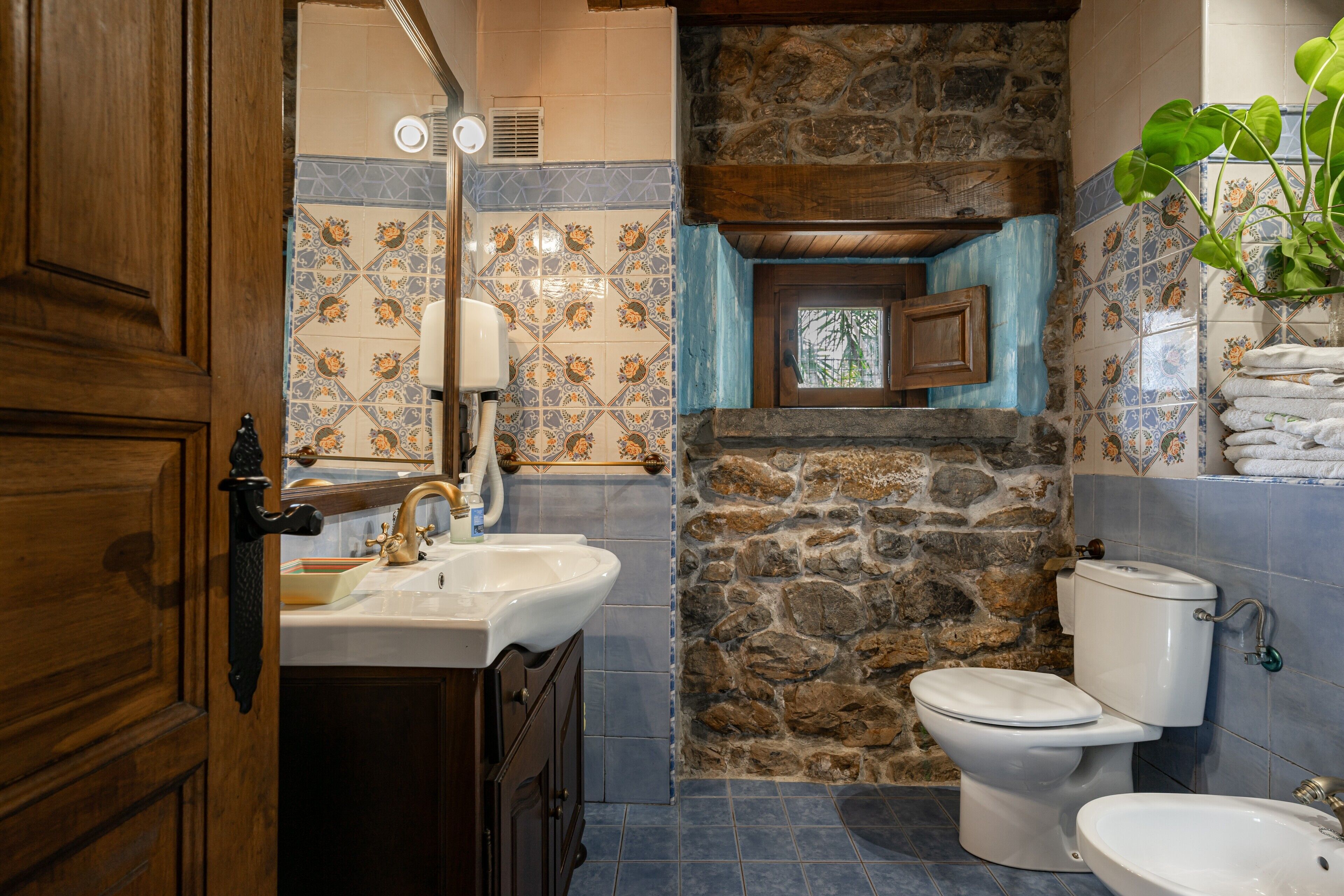 Ein Badezimmer mit Steinwand, Holztür, Waschbecken, Toilette und Bidet.