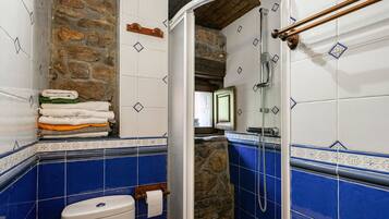 A bathroom with a stone wall, a toilet, a sink, and a shower.