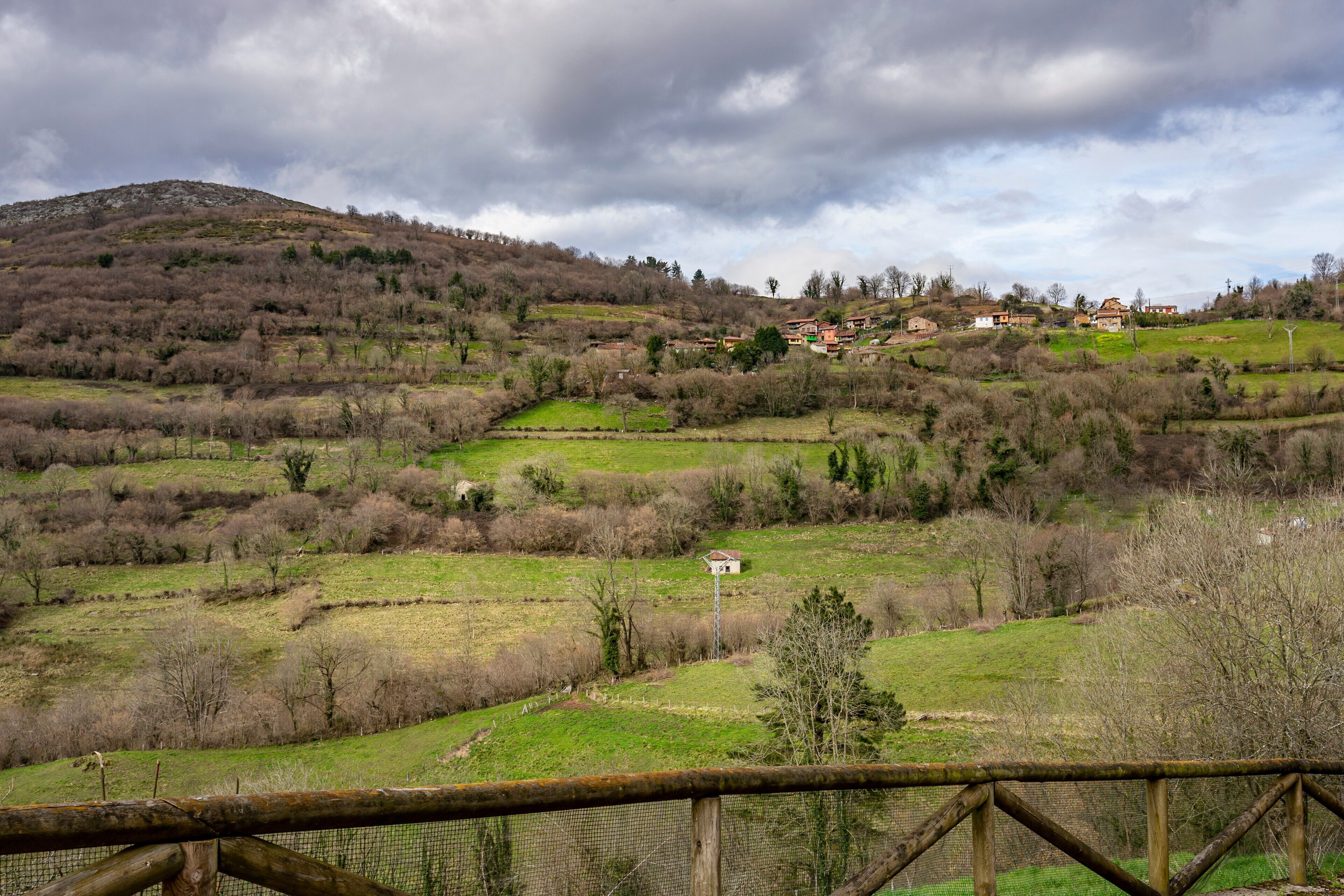 A rural landscape with rolling hills, sparse vegetation, and a few houses in the distance.
