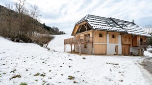 A wooden chalet with a balcony, set on a snowy hillside.