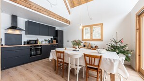 A modern kitchen with dark cabinets, a wooden ceiling, and a dining area with a white table and chairs.