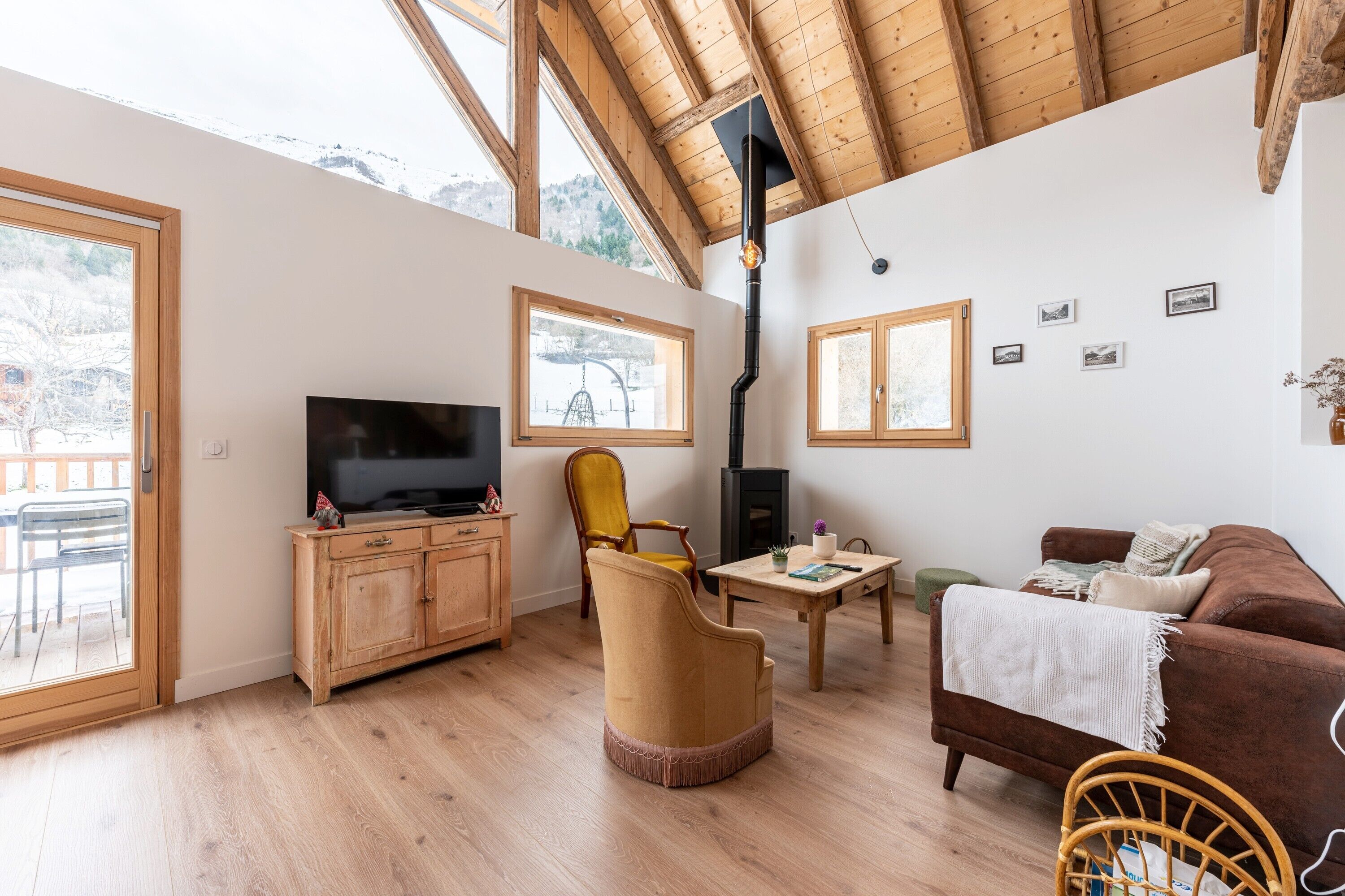 Een gezellige woonkamer met houten vloeren, een bank, een fauteuil, een televisie, een open haard en grote ramen.
