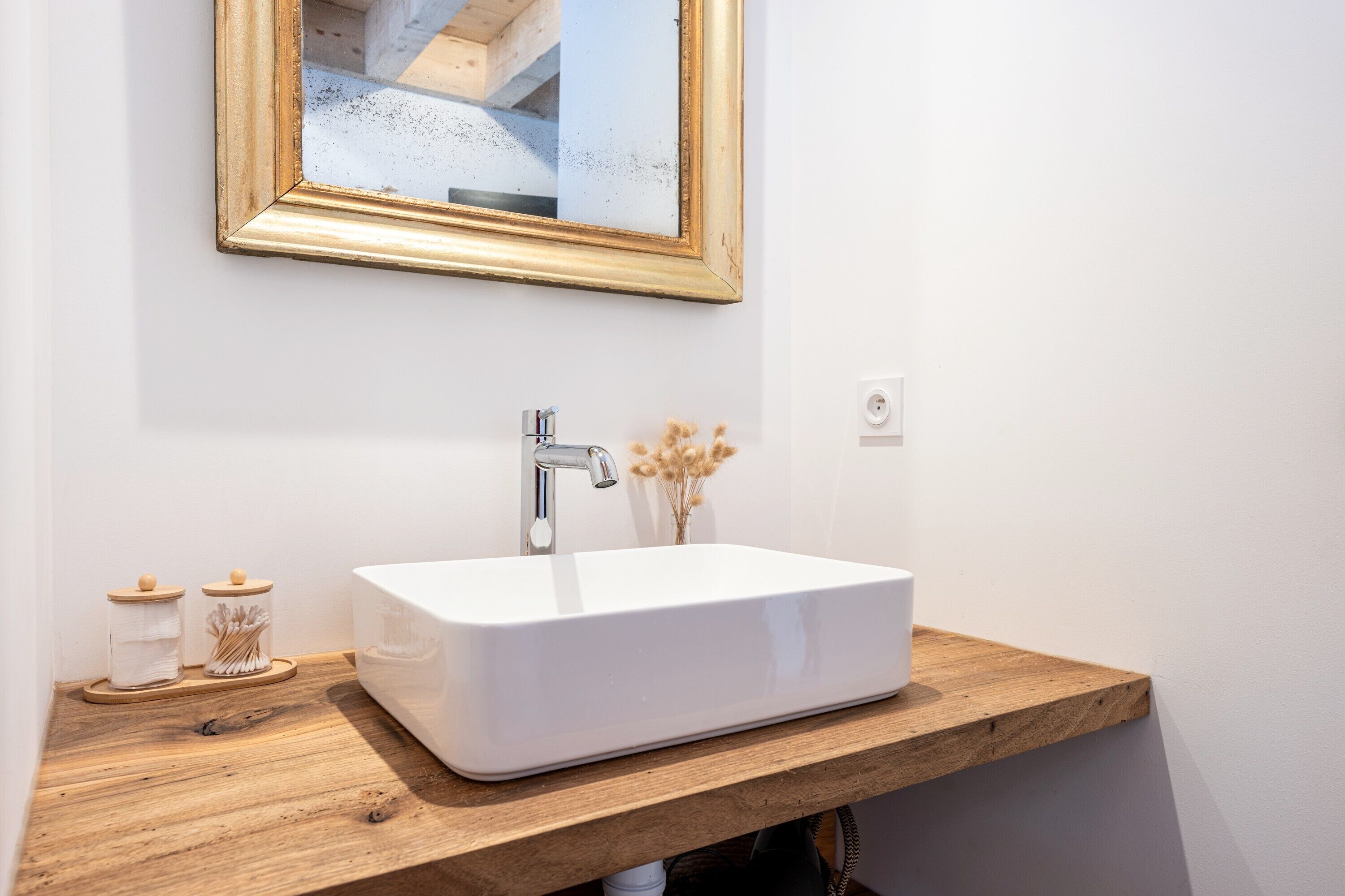 A bathroom with a white sink, wooden countertop, and a mirror with a gold frame.