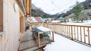 A wooden deck with a table and chairs, a wooden railing, and a snowy mountain backdrop.