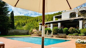 A pool area with lounge chairs, a pergola, and a stone wall. - Villa 'Ses Casetes Ibiza' with Mountain View, Wi-Fi and Air Conditioning (Illes Balears)