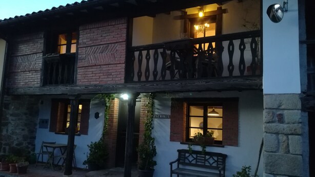 Een gebouw met twee verdiepingen, een balkon, een bankje en potplanten.