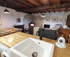 Een keuken met een grote gootsteen, een houten tafel, een stenen muur, een open haard en een televisie.