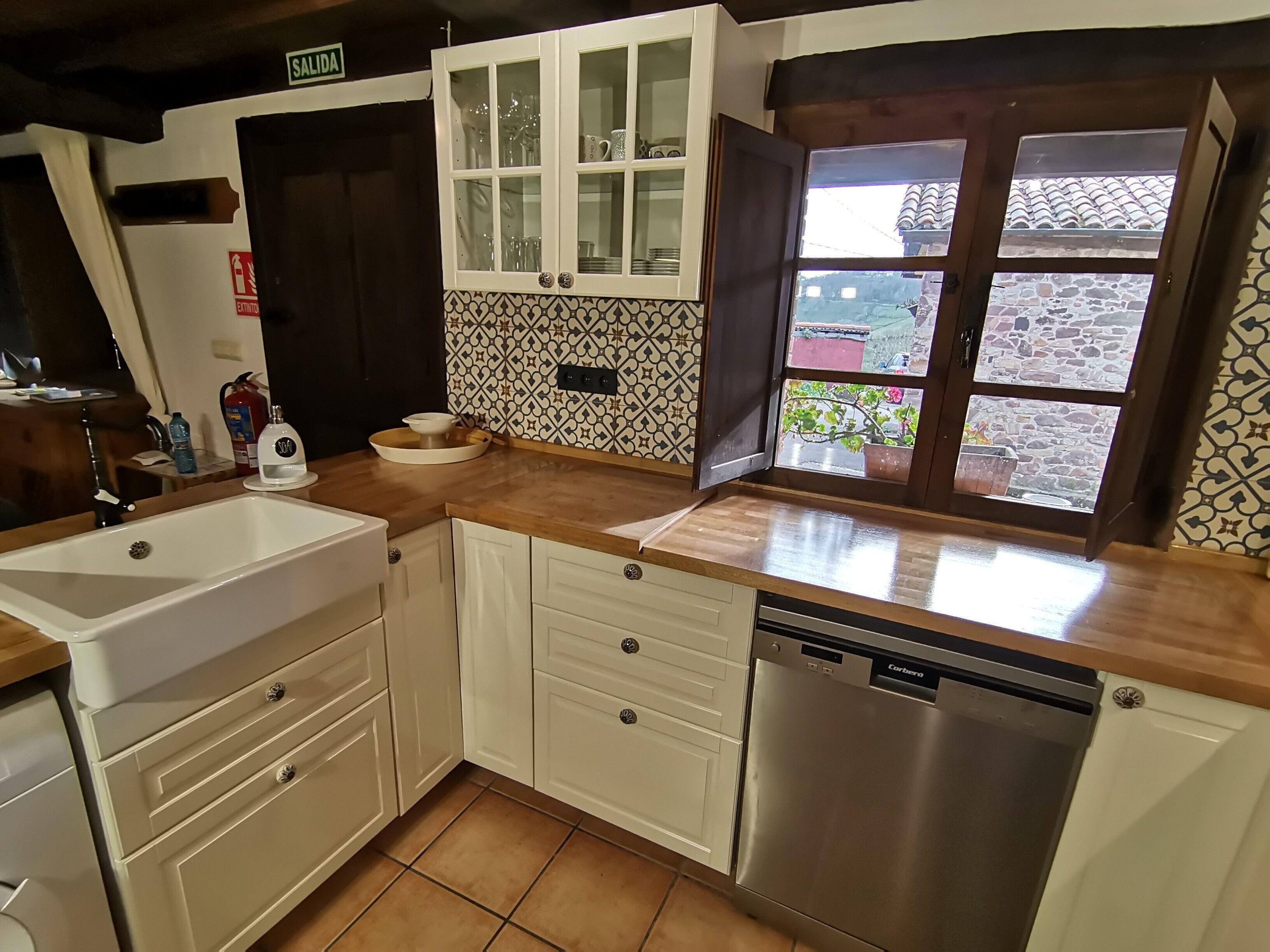 Una cocina con armarios blancos, lavavajillas y ventana con vistas al exterior.