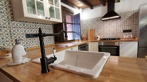 Een keuken met een witte spoelbak, zwarte kraan, houten aanrechtblad, decoratieve spatwand en een raam met uitzicht.