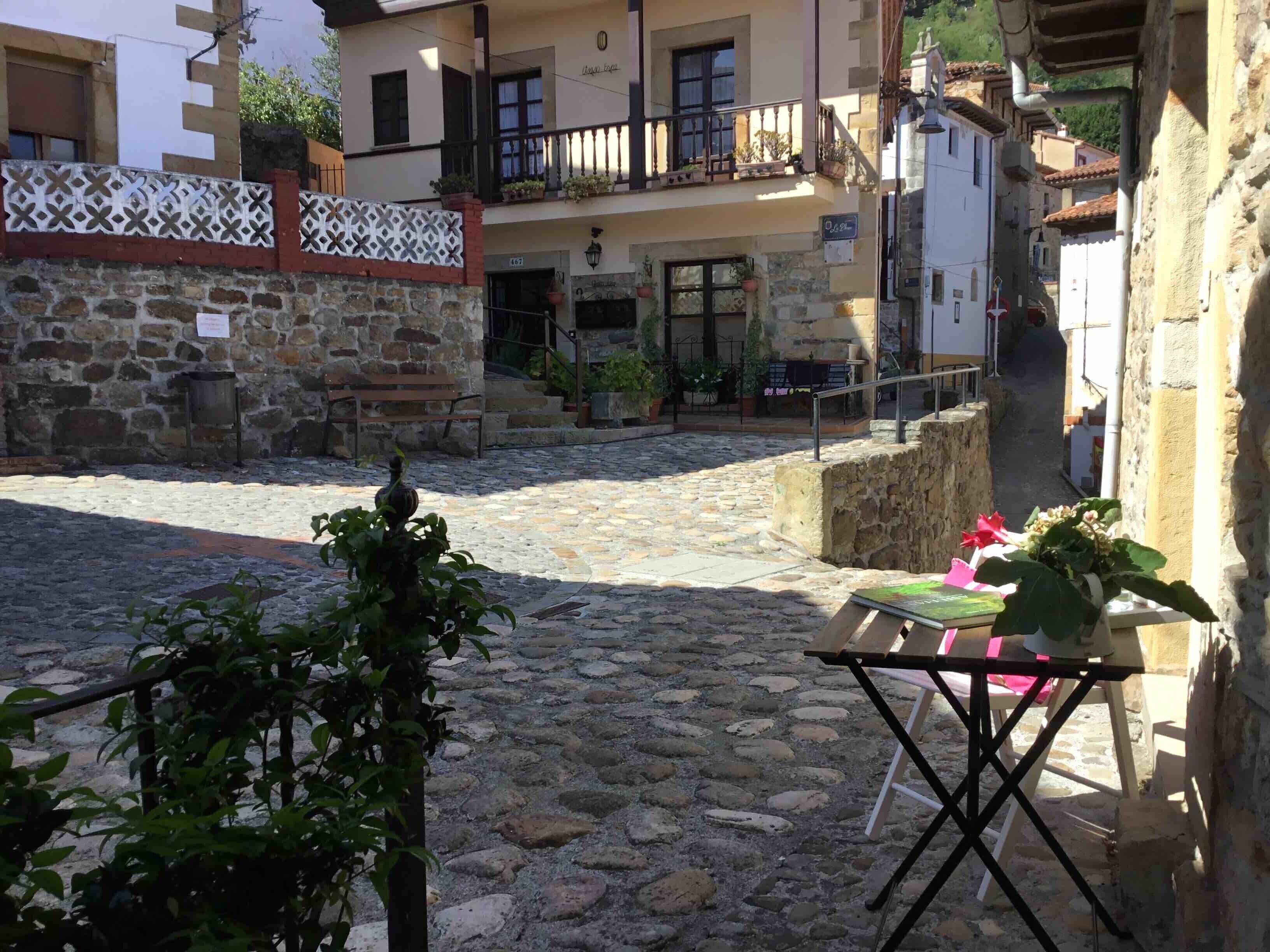 Un patio empedrado con un banco, una mesa con una silla y plantas en macetas.