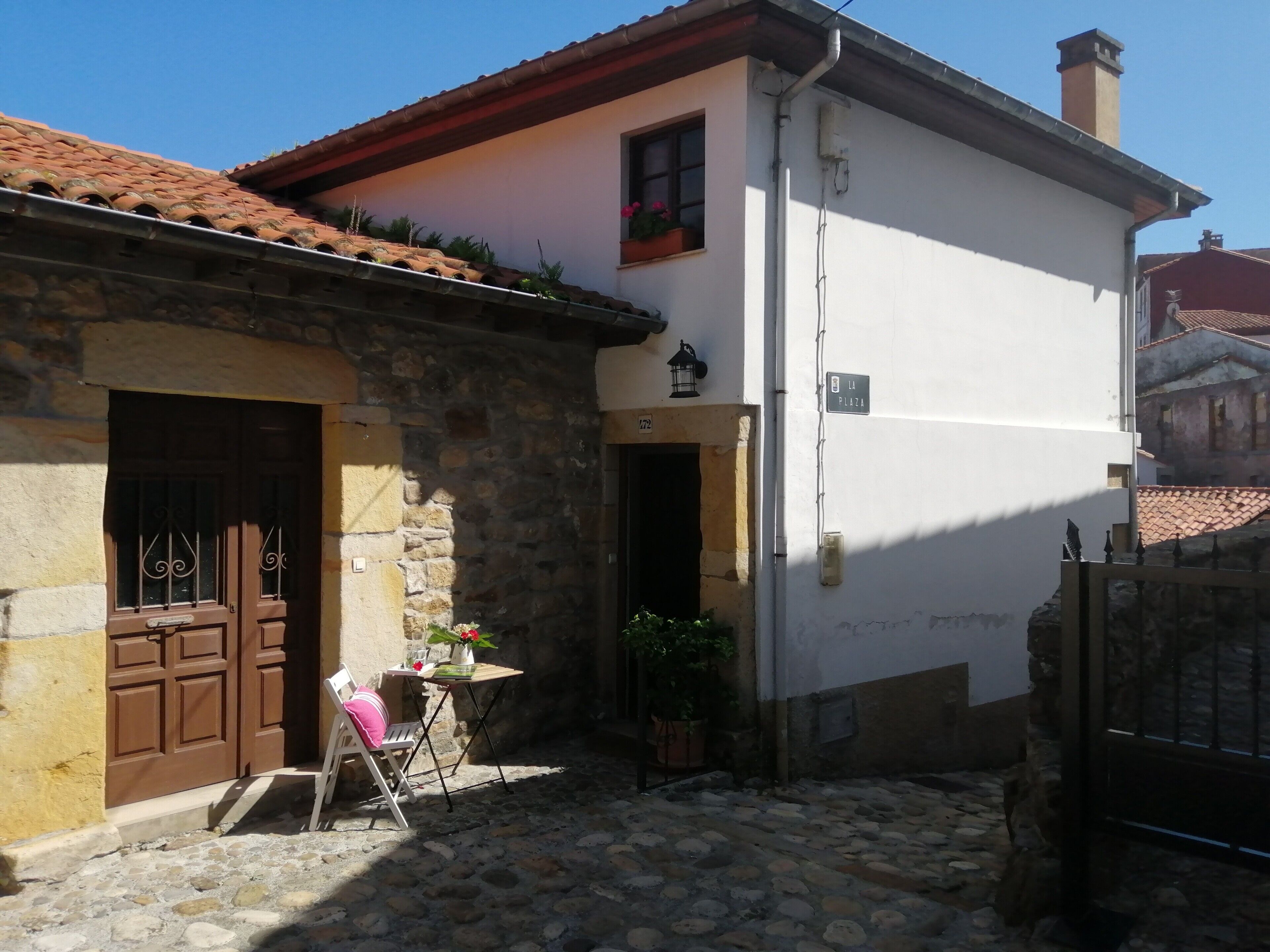 A stone building with a brown door, a small table with a chair, and a potted plant.