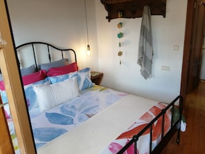 A bed with a floral bedspread, a wooden headboard, a nightstand with a lamp, and a wall-mounted towel rack. - Holiday Home 'El Canto De Las Gaviotas' with Sea View, Balcony and Wi-Fi (Lastres)