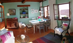 A cozy living room with a dining table, chairs, a sofa, and a window with curtains. - Holiday Home 'El Canto De Las Gaviotas' with Sea View, Balcony and Wi-Fi (Lastres)