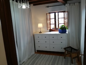 A room with a white dresser, a lamp, a window with curtains, a small stool, and a patterned rug. - Holiday Home 'El Canto De Las Gaviotas' with Sea View, Balcony and Wi-Fi (Lastres)