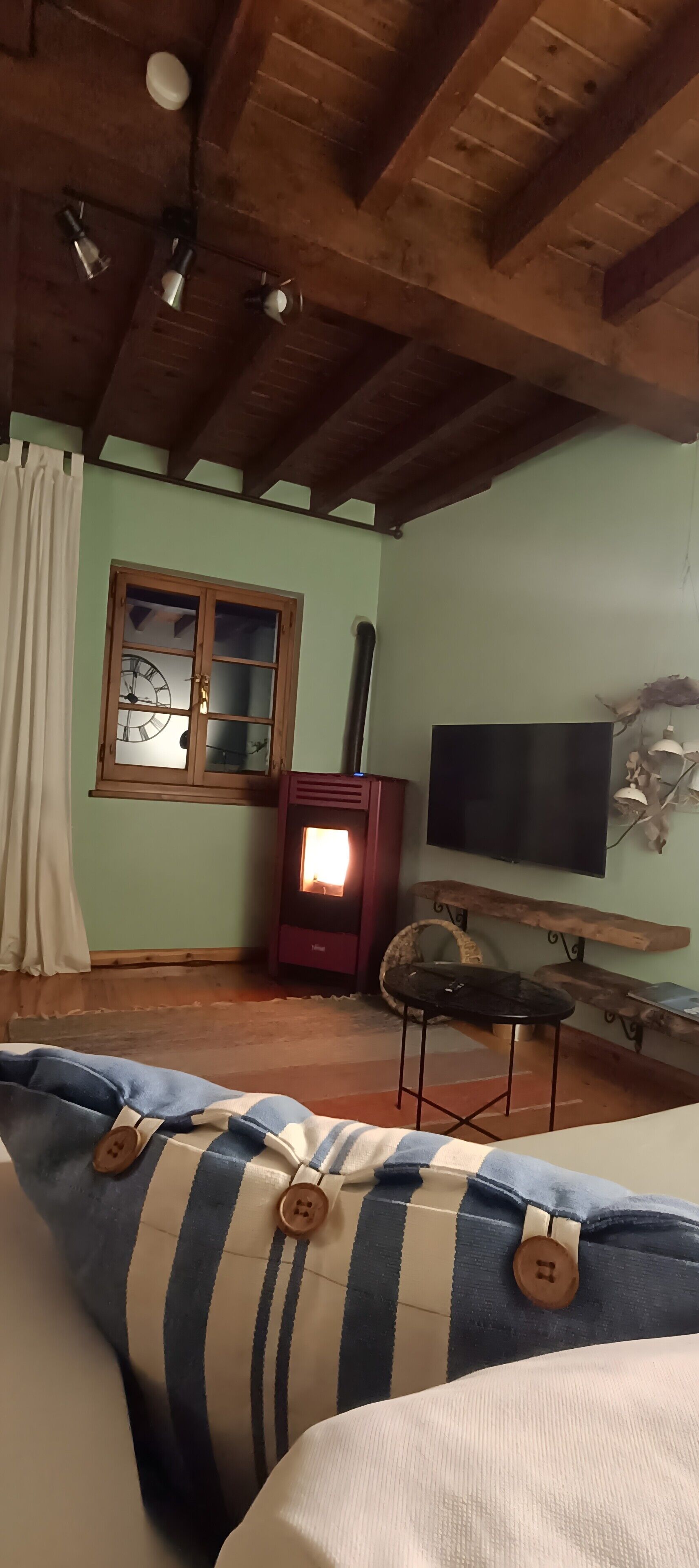 Une pièce chaleureuse avec un plafond en bois, une cheminée, une télévision et une fenêtre avec des rideaux.