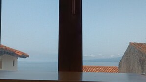 Une vue par la fenêtre sur un bâtiment doté d’un toit recouvert de tuiles et d’un mur sobre.