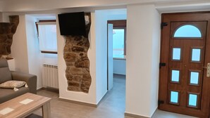 Un salon avec un mur d’accent en pierre, un téléviseur fixé au-dessus, une porte en bois avec des panneaux de verre et une vue sur une autre pièce.