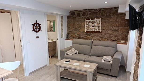 Un salon comprenant un canapé, une table basse, un téléviseur fixé au mur et un mur en pierre.