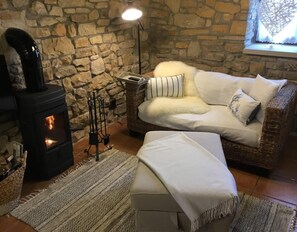 Una habitación acogedora con una pared de piedra, chimenea, sofá de mimbre y un banco blanco.