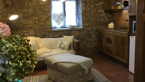 Un ambiente accogliente con parete in pietra, divano, un piccolo tavolo e angolo cottura.