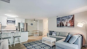 A modern apartment with a kitchen, dining area, and living room. It includes a microwave, refrigerator, and a sofa with a patterned rug.