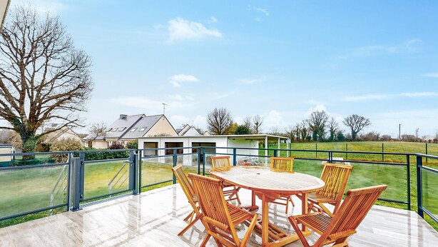 A covered outdoor patio with a round table and six wooden chairs, surrounded by a metal railing. - 3 bedroom nice home in Arzal (Arzal)