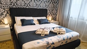 Una cama bien hecha con almohadillas, una mesita de noche con lámpara y un edredón estampado con motivos florales.