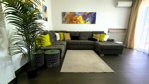Una sala de estar moderna con un sofá modular, una planta grande en maceta y un cuadro en la pared.
