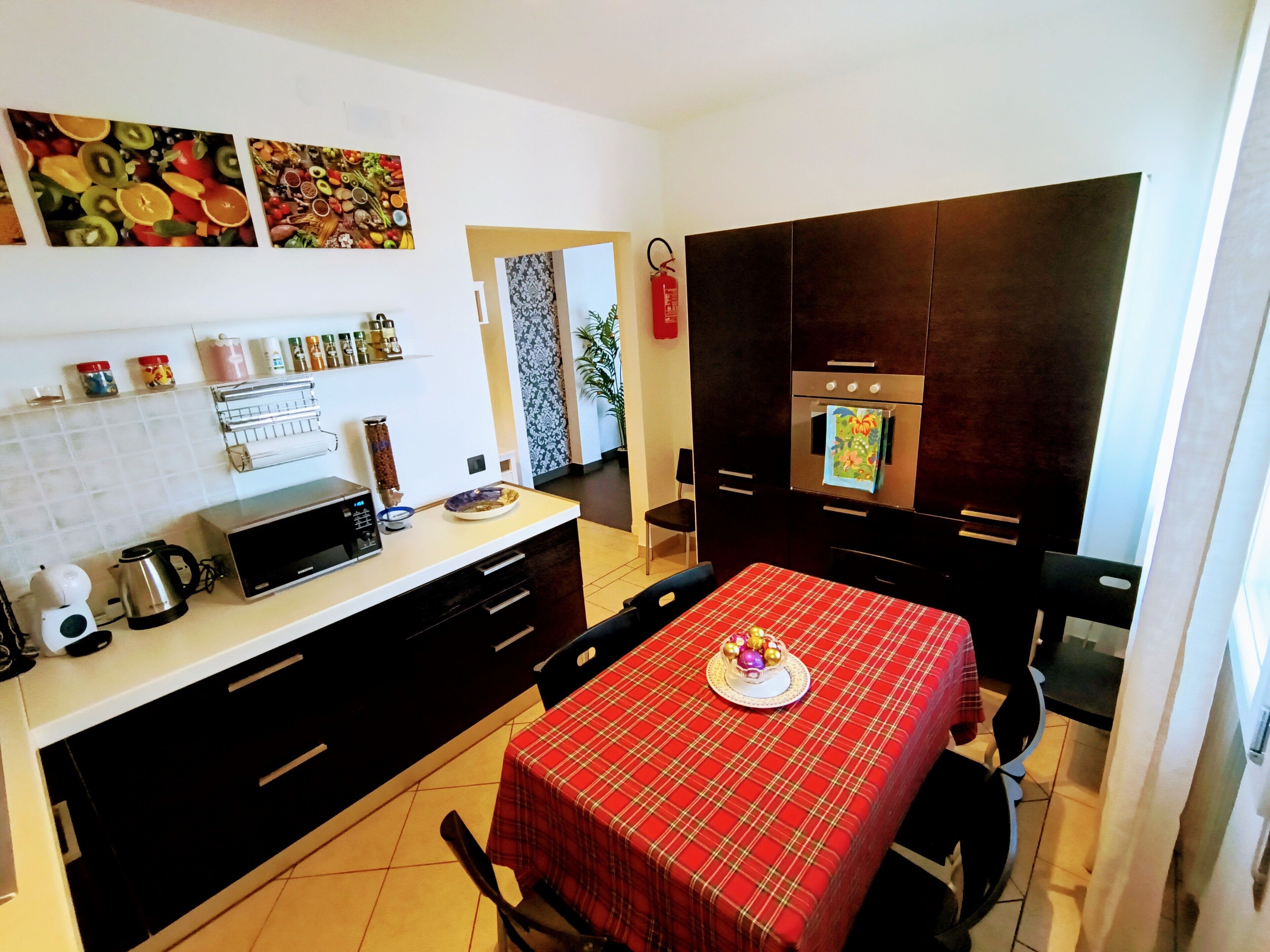 A compact kitchen with a microwave, kettle, and a red checkered tablecloth.