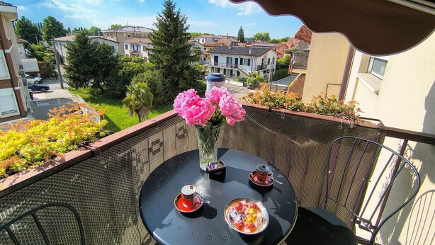 Un balcón con una mesa, sillas, un florero y vistas a edificios residenciales.