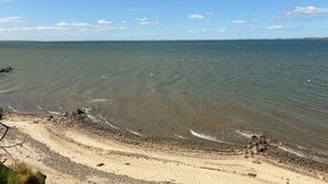 A beach with clear water, pebbles, and a distant shoreline.