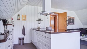 A compact kitchen with white cabinetry, a wooden countertop, and a built-in stove. There is a trash can and a hanging towel.