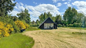 A cabin with a sloped roof, surrounded by a grassy field and dense trees.