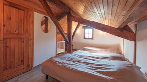Una camera da letto con soffitto a falde, travi in legno, una culla e un letto con copripiumino bianco.