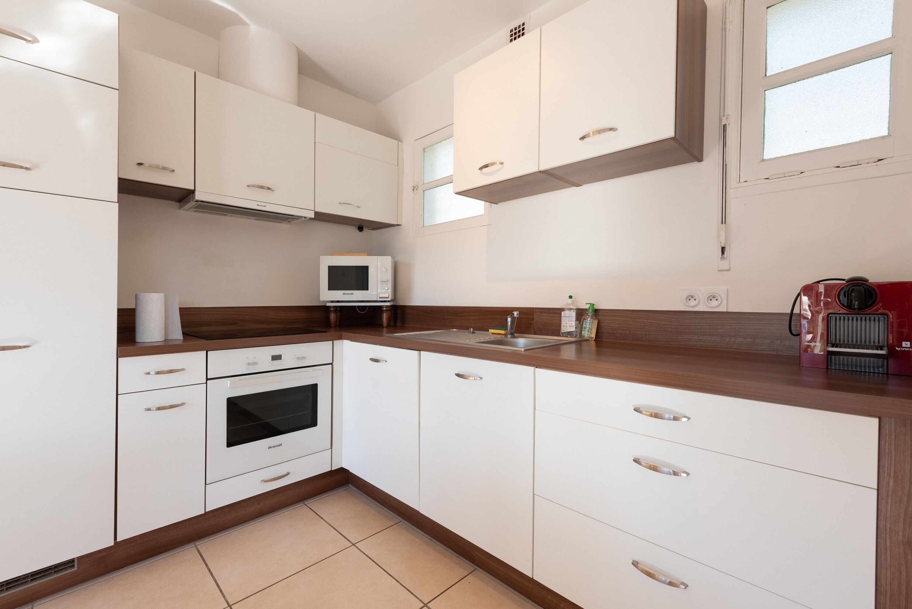 Una cocina moderna con armarios blancos, un microondas, un horno y un electrodoméstico rojo sobre la encimera.