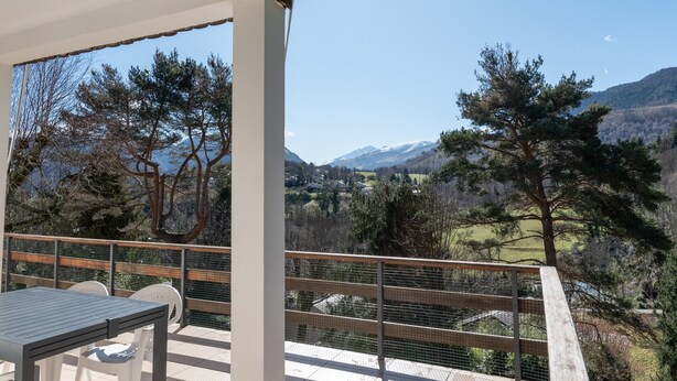 Un balcone con tavolo e sedie, affaccia su un paesaggio montuoso.