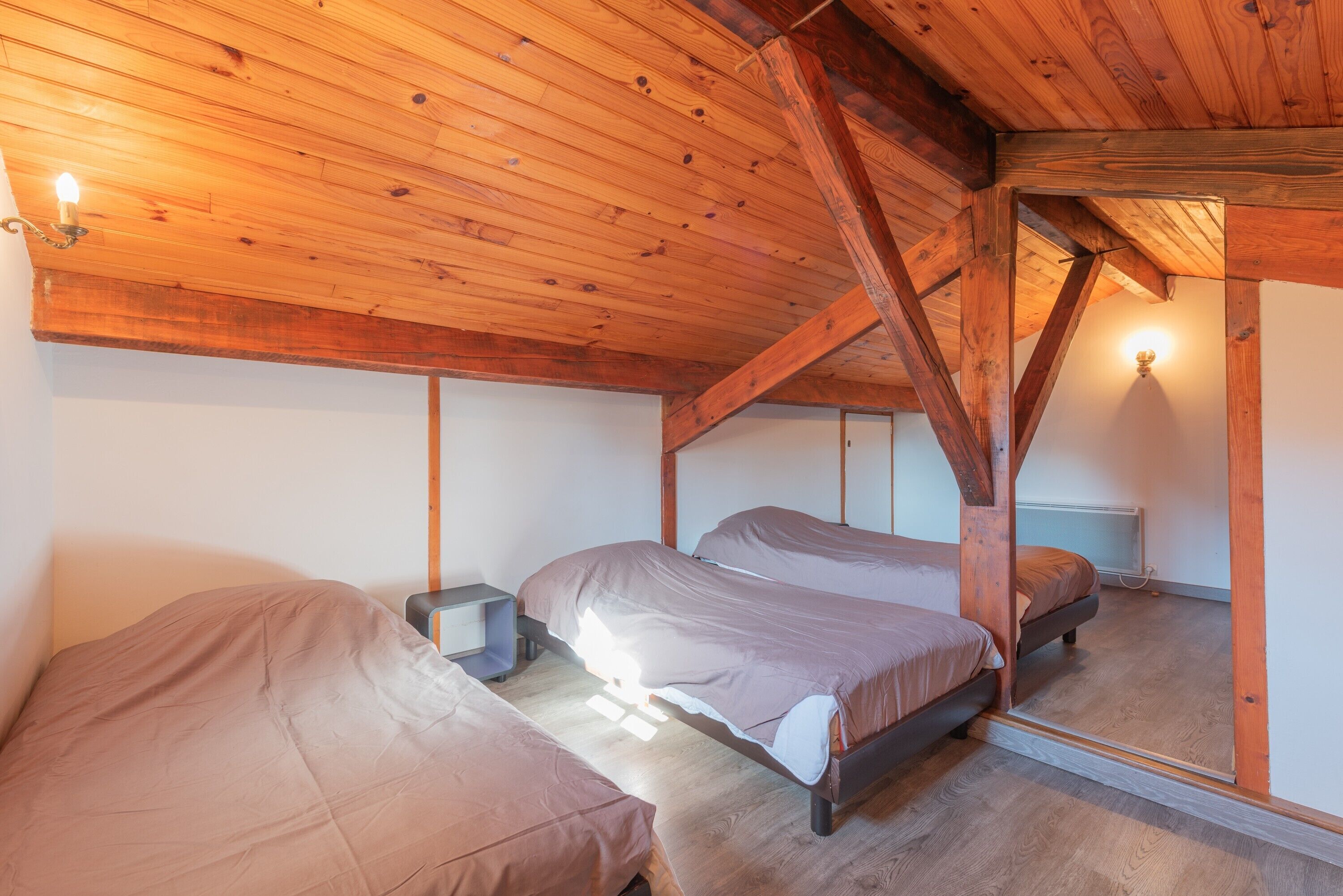 Une chambre avec deux lits, des poutres apparentes en bois au plafond et un luminaire fixé au mur.
