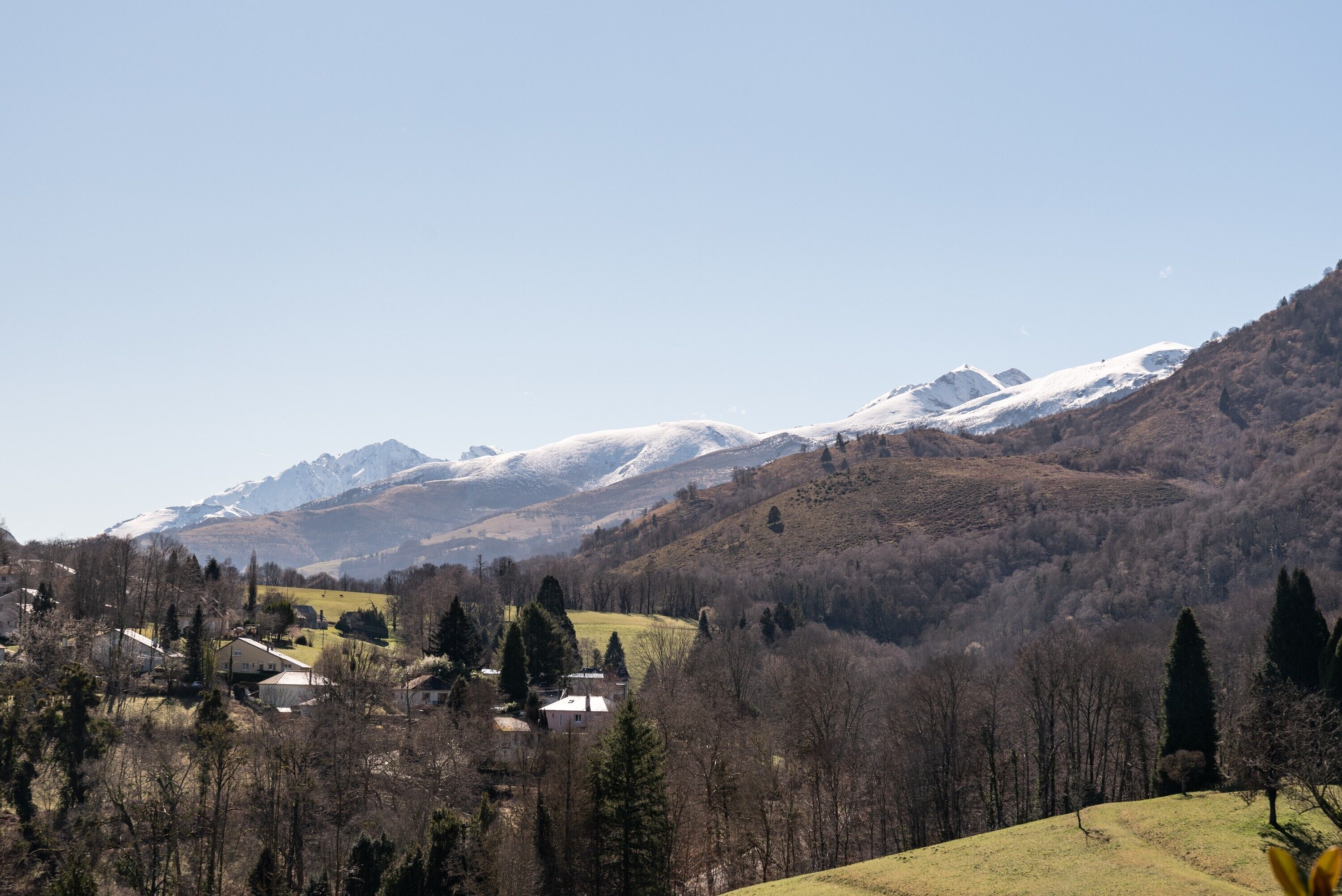 A mountainous landscape with snow-capped peaks, a valley with houses, and a clear sky.