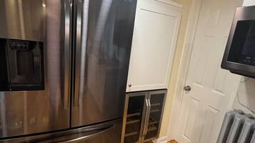 Ein Edelstahl-Kühlschrank mit Gefrierfach, darüber eine Mikrowelle, und im Hintergrund eine weiße Tür.