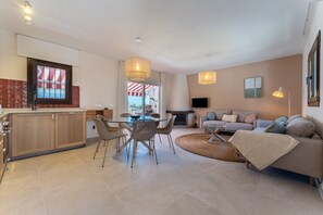 Een moderne woonkamer met een bank, eettafel en stoelen. Er is een keuken met kastjes en een raam.