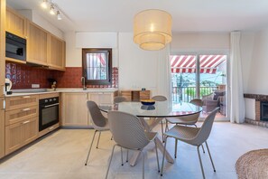 A modern kitchen with wooden cabinets, a built-in oven, and a dining area with a glass table and wicker chairs. - Holiday Home 'Feliz' with Sea View, Wi-Fi and Air Conditioning (Benalmadena)