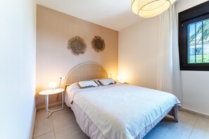Een slaapkamer met een bed, nachtkastjes, wanddecoratie en een raam met gordijnen.