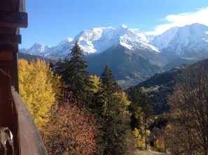 Un chalet de montagne offrant une vue sur les sommets enneigés et les arbres aux couleurs automnales.