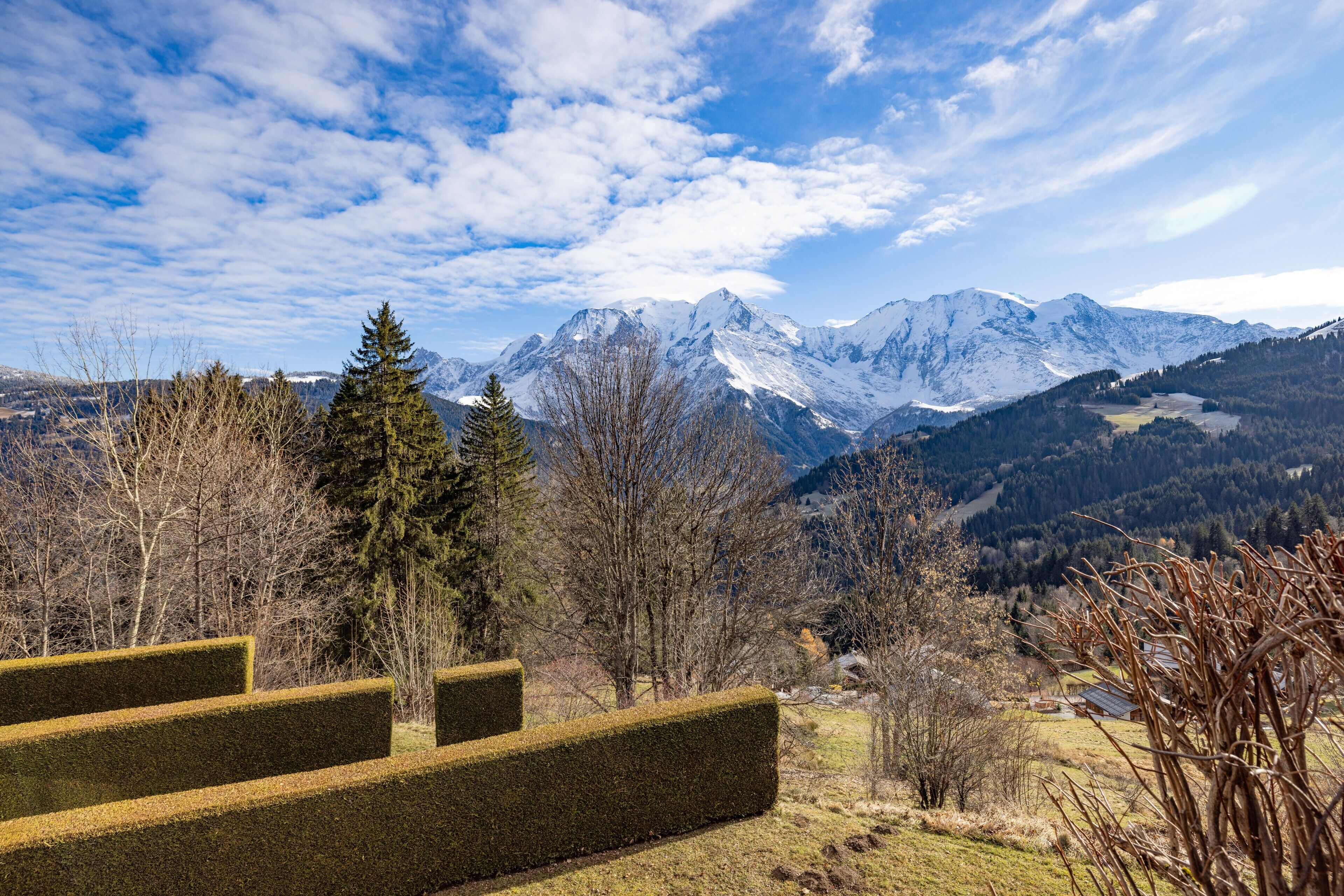 A mountainous landscape with snow-capped peaks, a clear sky, and a few trees.