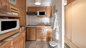 A compact kitchen with wooden cabinets, a microwave, a stove, and a sink. - Apartment "Vue Mont Blanc" (Saint-Gervais-les-Bains)
