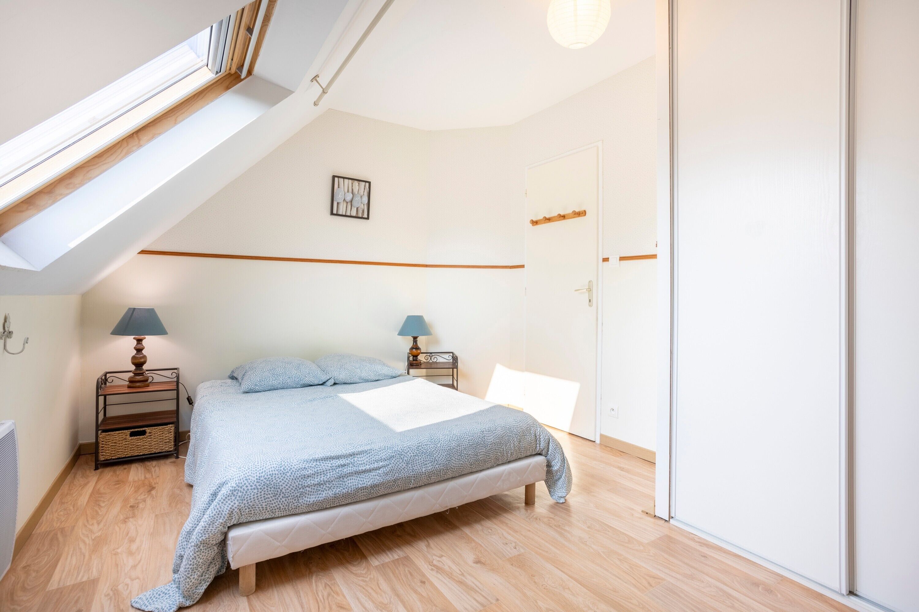 Ein Schlafzimmer mit schrägen Wänden, einem Bett, zwei Nachttischen mit Lampen, einem Wandbild und einem Kleiderschrank.