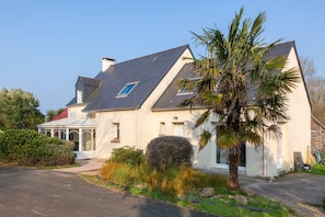 A two-story house with a sloped roof, a conservatory, and a palm tree in the front yard. - Holiday Home 'Grande Maison À 5min Des Plages' with Shared Pool, Terrace and Private Garden (Pouldreuzic)